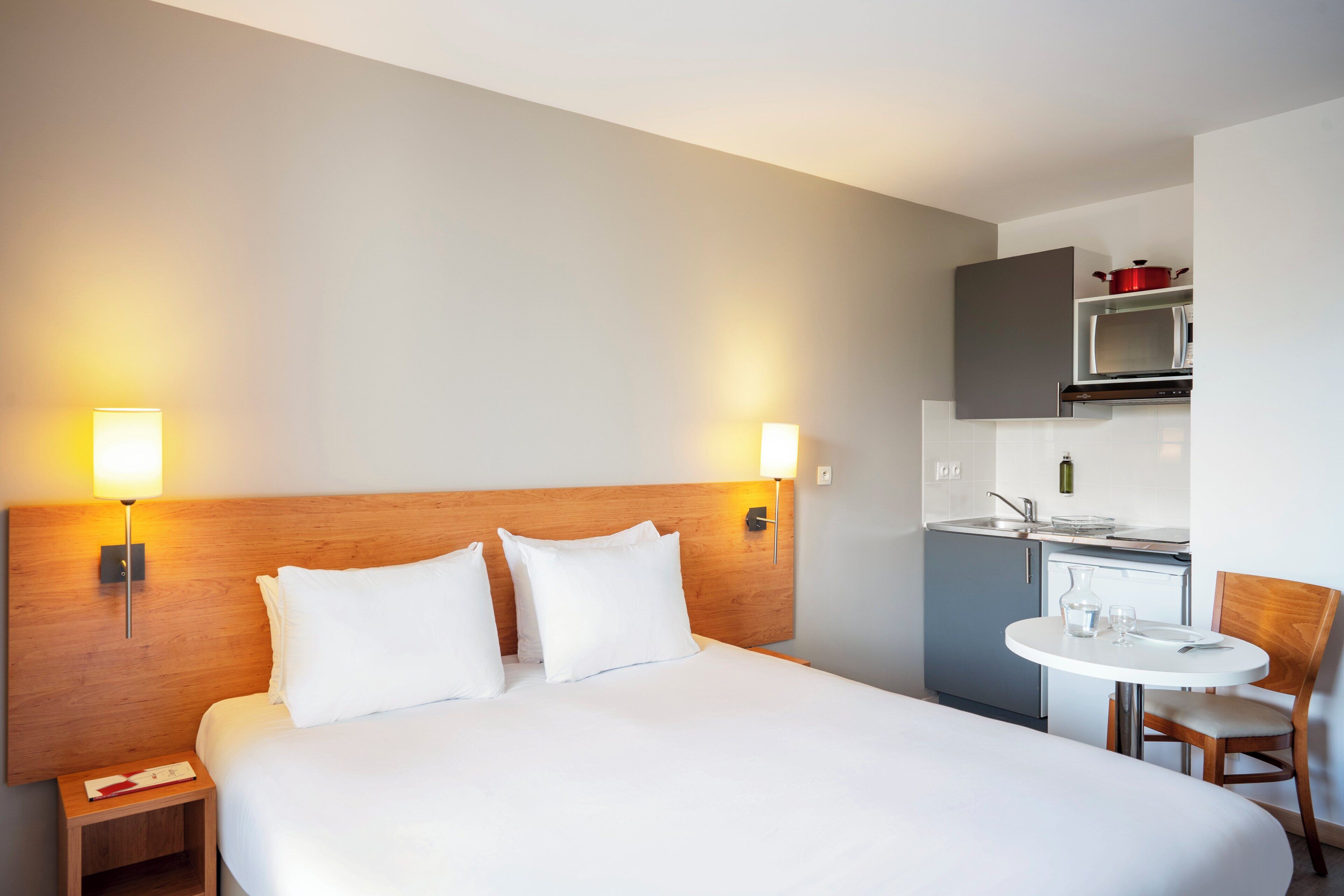 A hotel room with a large bed, bedside tables, a small kitchenette, and a dining area.