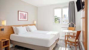 Hotelkamer met een groot bed, nachtkastjes, een bureau met stoel, een aan de muur bevestigde televisie en een raam met gordijnen.