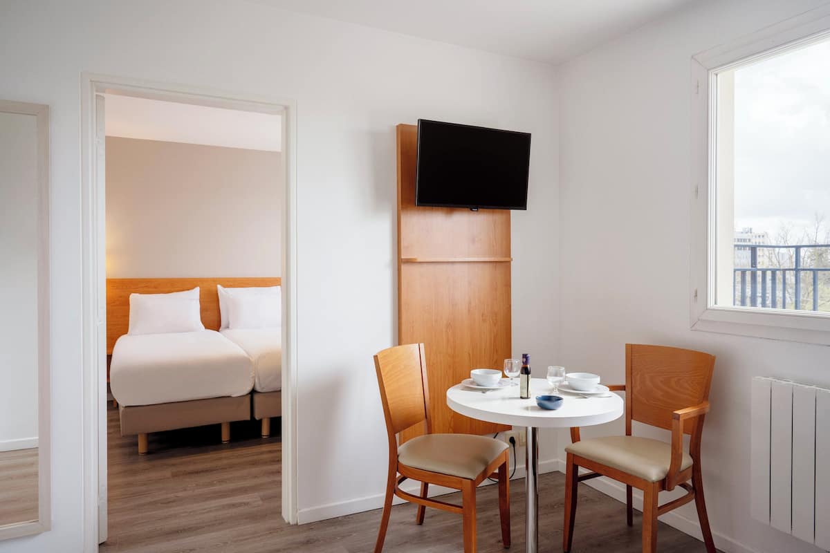 Ein Hotelzimmer mit einem Bett, zwei Stühlen, einem kleinen runden Tisch und einem an einer Holzplatte montierten Fernseher.