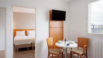 Une chambre d’hôtel comprenant un lit, deux chaises, une petite table ronde et un téléviseur fixé sur un panneau en bois.