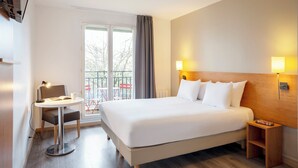 Hotelkamer met een groot bed, bedlampjes, een kleine tafel met stoel en uitzicht op het balkon.