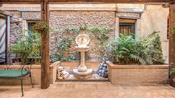 A courtyard with a stone wall, a wooden bench, a fountain, and various potted plants. - Residenza San Calisto (Rome)