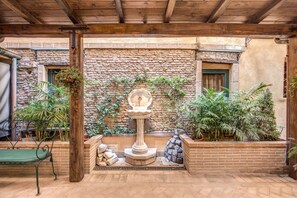 A courtyard with a stone wall, a wooden bench, a fountain, and various potted plants. - Residenza San Calisto (Rome)