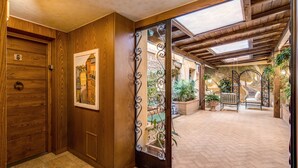 A wooden door with a number plate, a framed picture, and a decorative metal gate leading to an outdoor patio area with potted plants and a bench. - Residenza San Calisto (Rome)