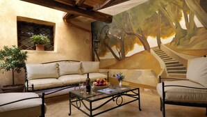 A cozy patio area with a sofa, armchairs, and a coffee table. There is a mural on the wall depicting a forest scene. - Residenza San Calisto (Rome)