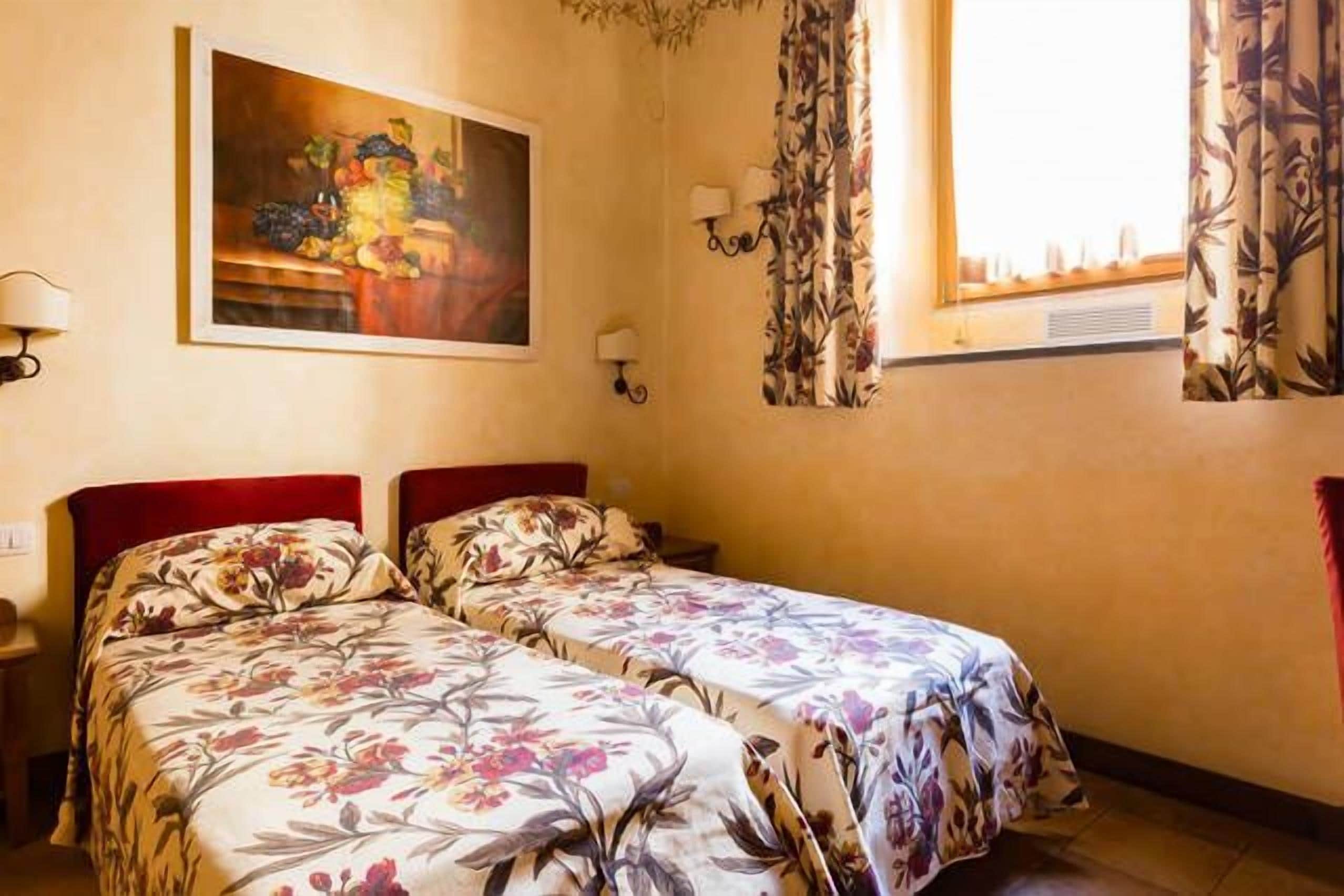 A room with two beds, a painting on the wall, and a window with curtains.