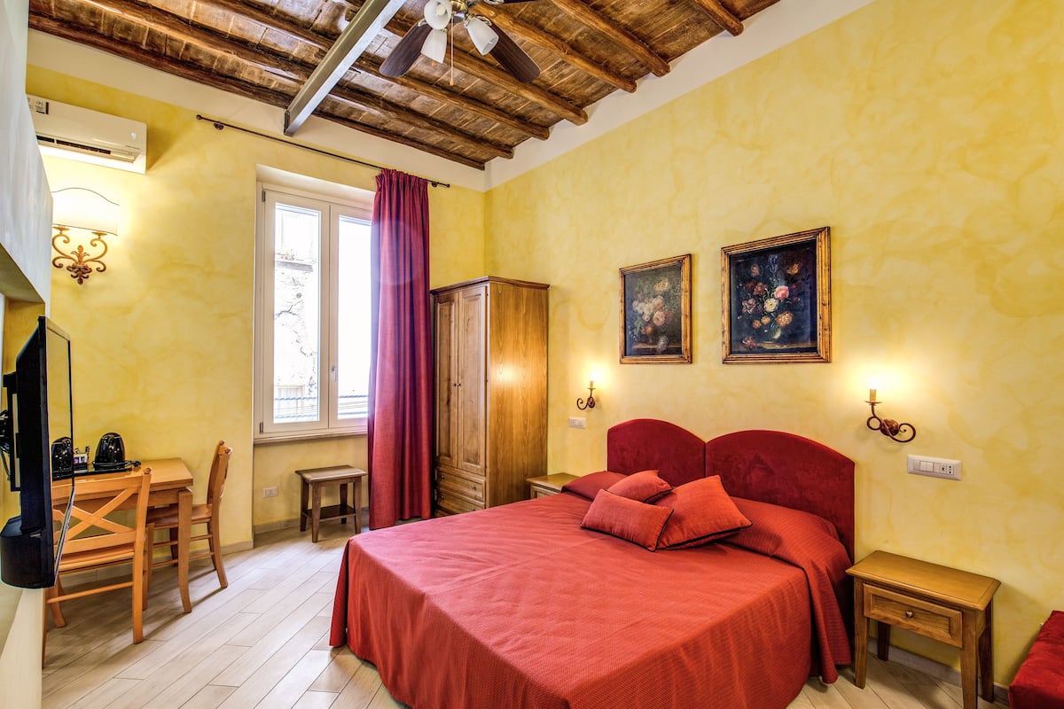 A bedroom with a wooden bed, a desk with a chair, a wardrobe, and a window with curtains.