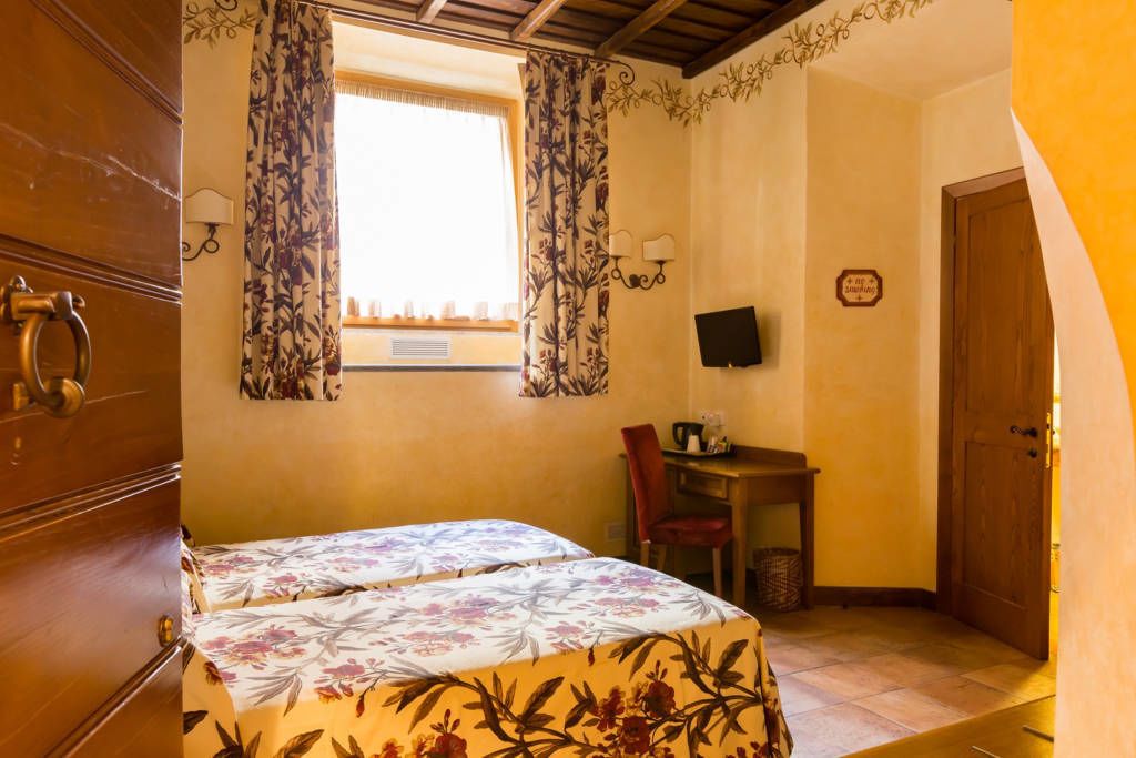 A room with a bed, a desk, a chair, a TV, and a window with curtains.