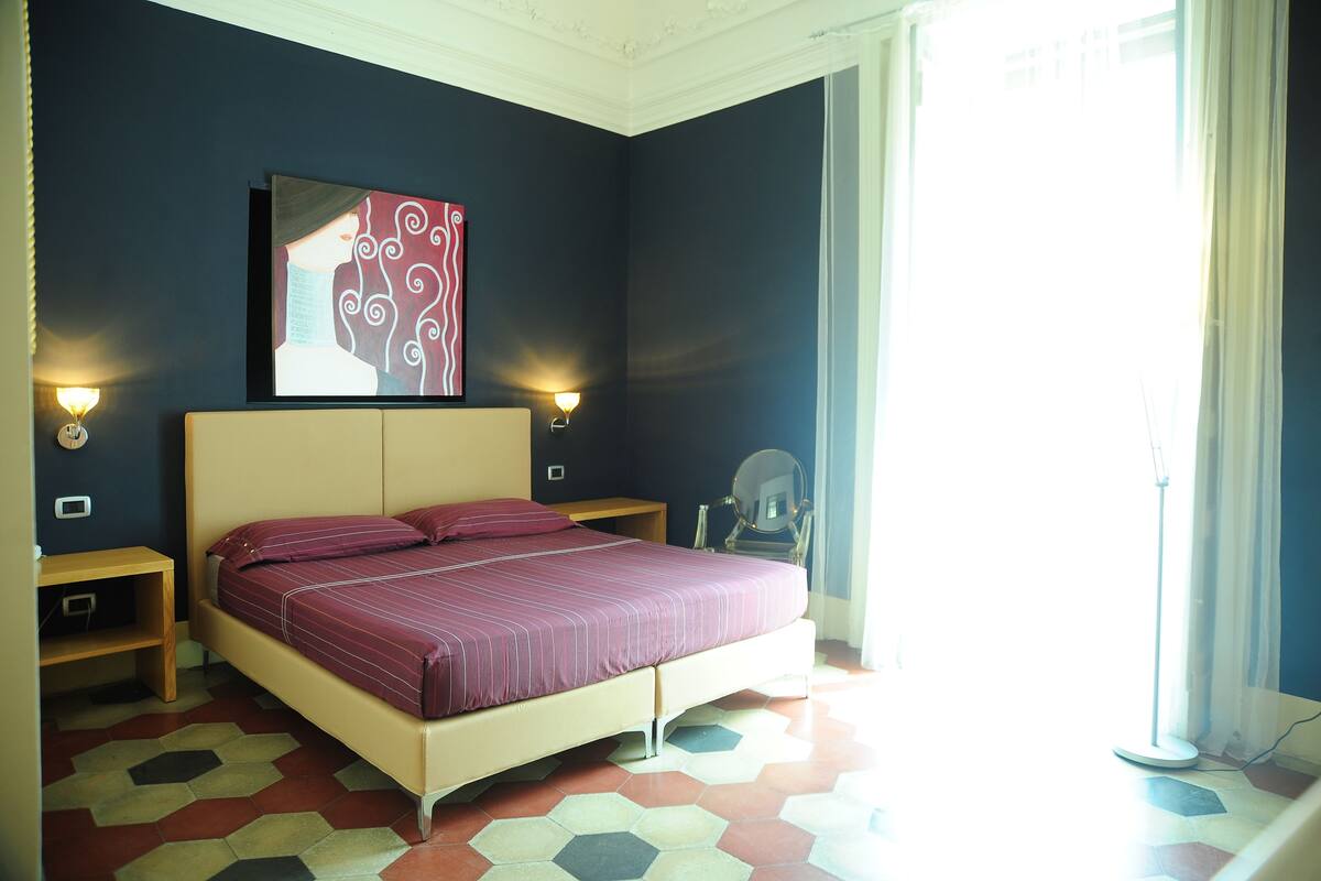 A bedroom with a bed, two bedside tables, a mirror, and a painting on the wall.