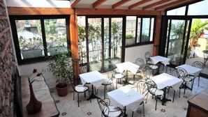 An indoor patio with tables and chairs, large windows, and potted plants. - Sangiuliano 114 (Catania)