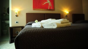 A neatly made bed with folded towels and a single rose, a red abstract painting on the wall, and two wall-mounted lamps. - Sangiuliano 114 (Catania)