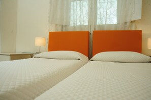 A room with two beds, each with white bedding and orange headboards. There is a nightstand with a lamp on the left side. - Sangiuliano 114 (Catania)