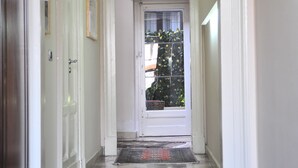 A hallway with a door on the left, a window with a view of greenery, and a door at the end. - Sangiuliano 114 (Catania)