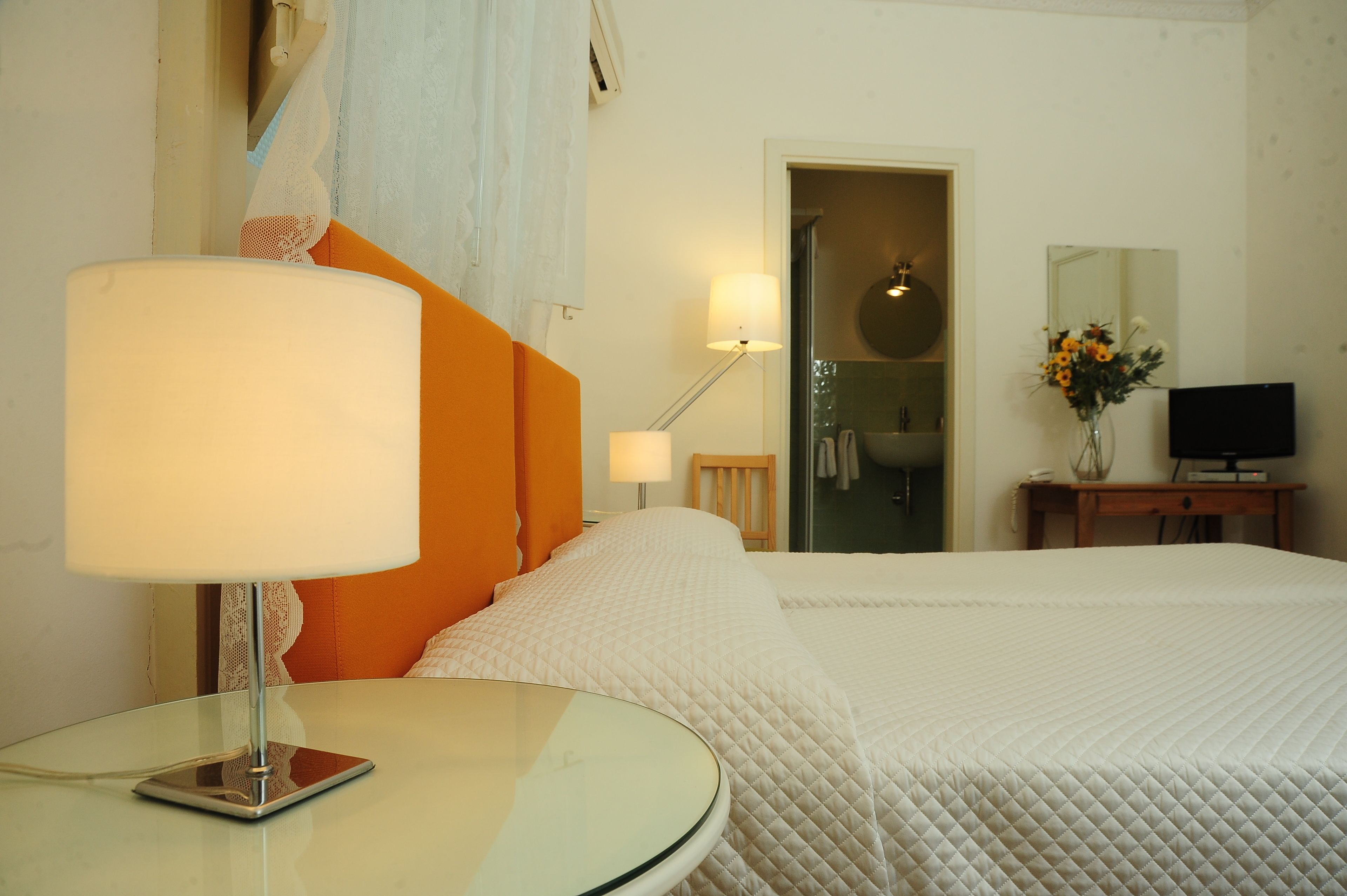 A hotel room with a bed, a bedside table with a lamp, a television, and a bathroom visible through an open door.