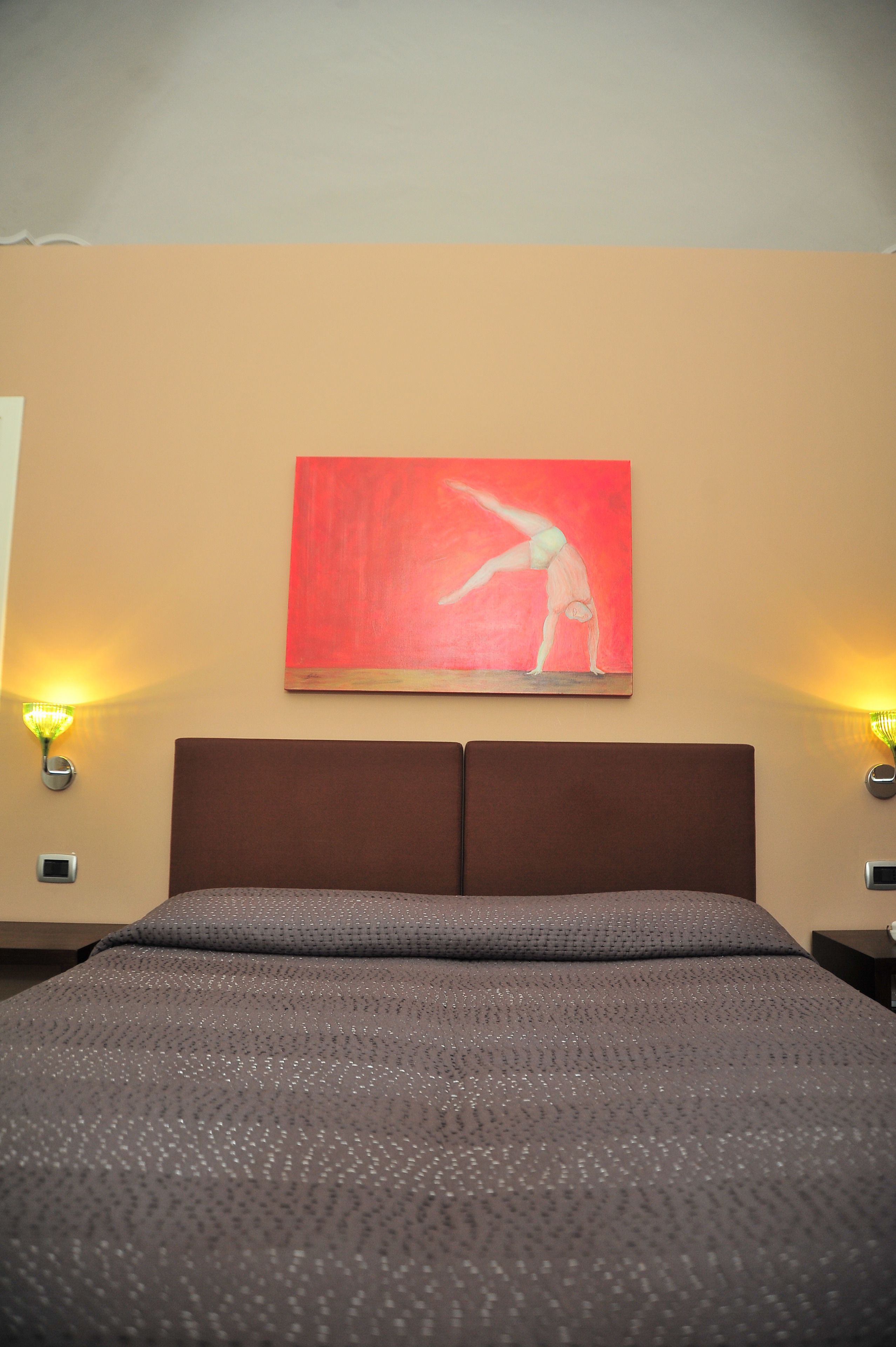 Une chambre d’hôtel avec un lit, un tableau au mur et deux lampes fixées au mur.