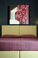 Una cama con colcha a rayas y dos almohadas, un cuadro enmarcado sobre la cama y una pared oscura.