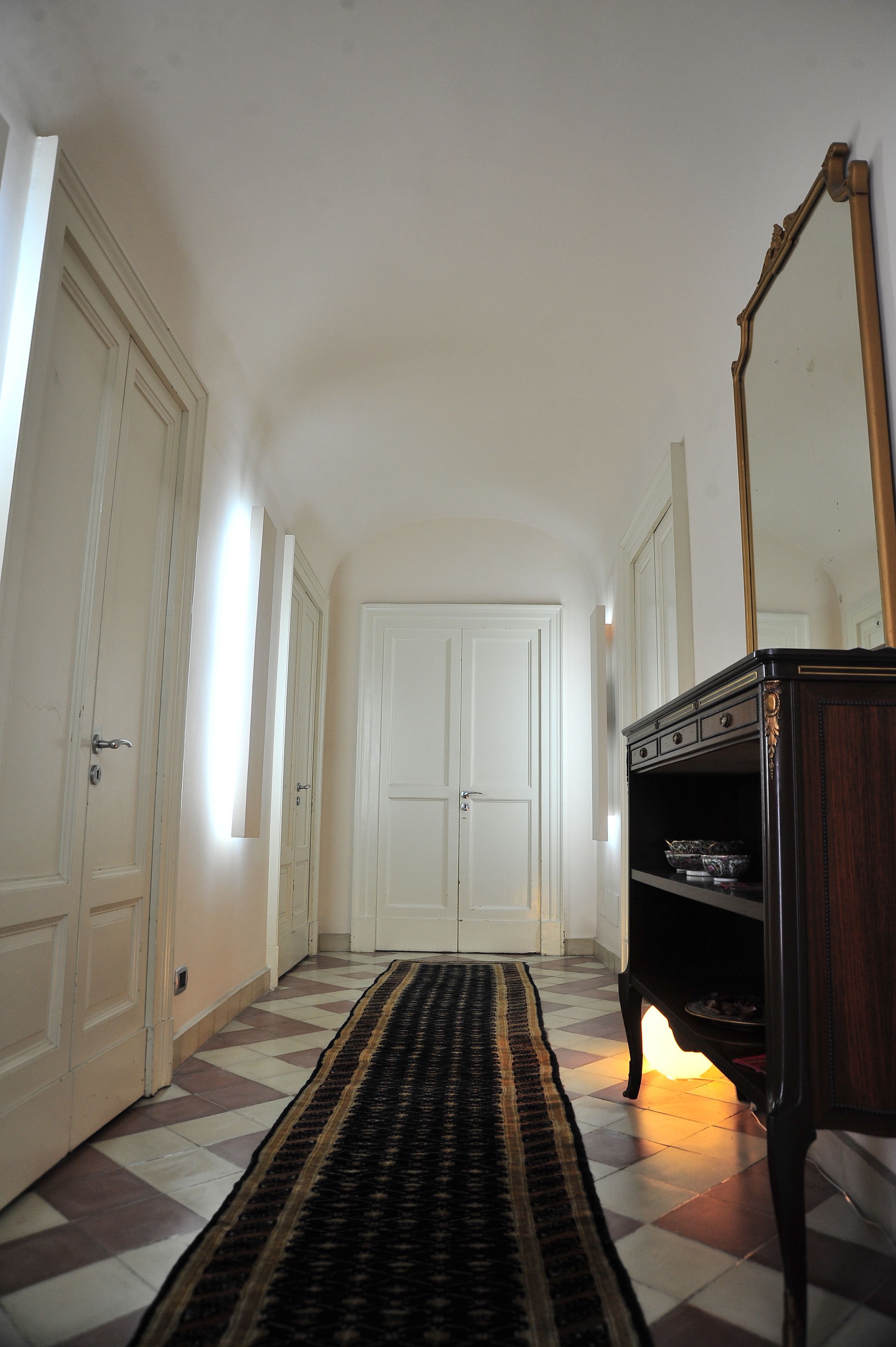A hallway with a checkered floor, a dark wooden dresser with a mirror, and white doors.