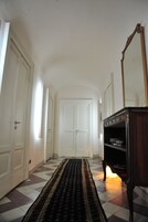 Un corridoio con pavimento a scacchi, un comò in legno scuro con specchio e porte bianche.