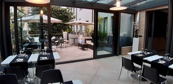 Un área de comedor al aire libre con mesas, sillas, sombrillas y vistas al entorno verde.