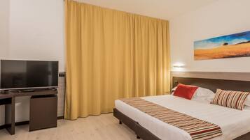 A hotel room with a bed, a TV, a desk, and a painting on the wall.