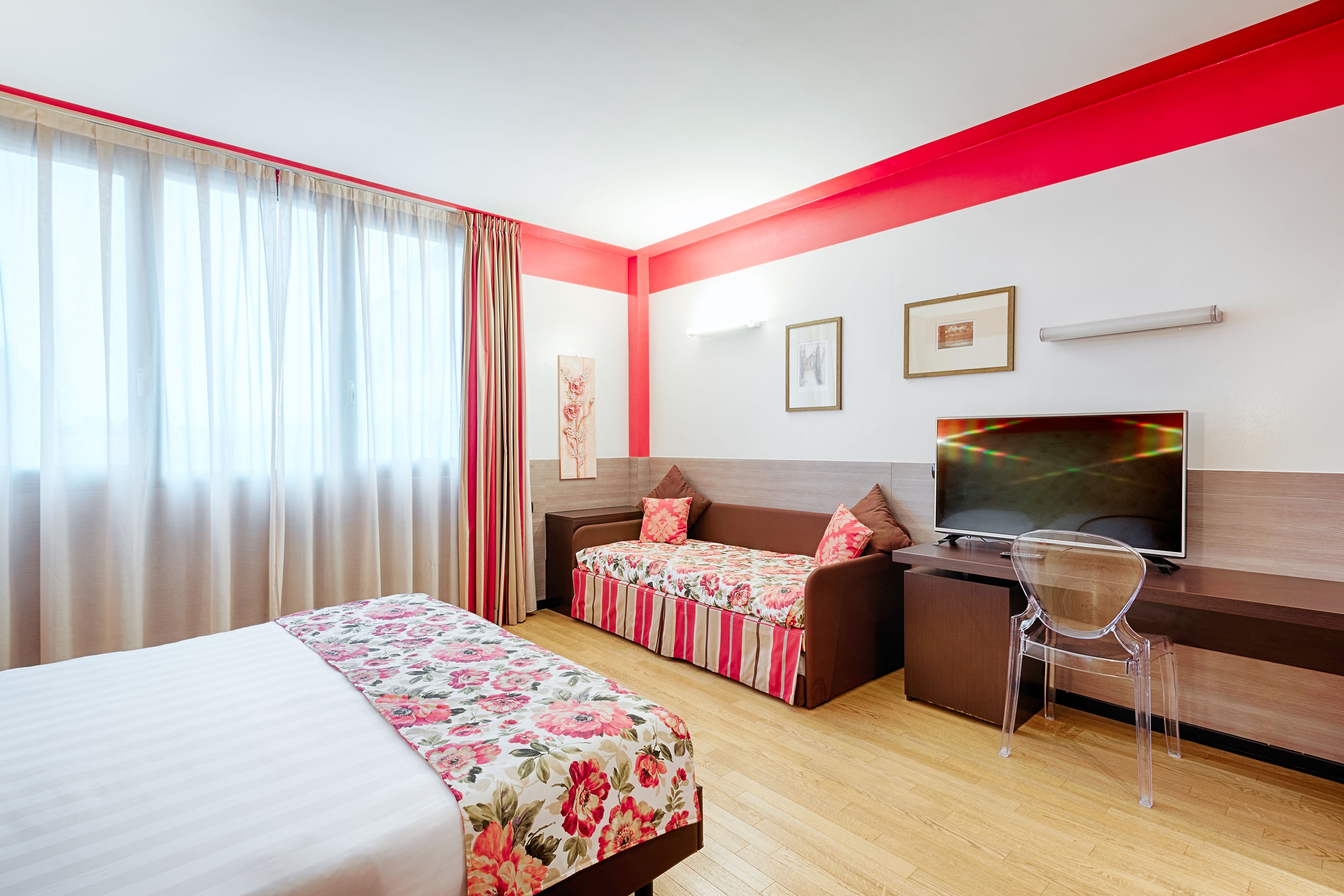 Ein Hotelzimmer mit zwei Betten, einem Schreibtisch mit Fernseher und einem Sessel.