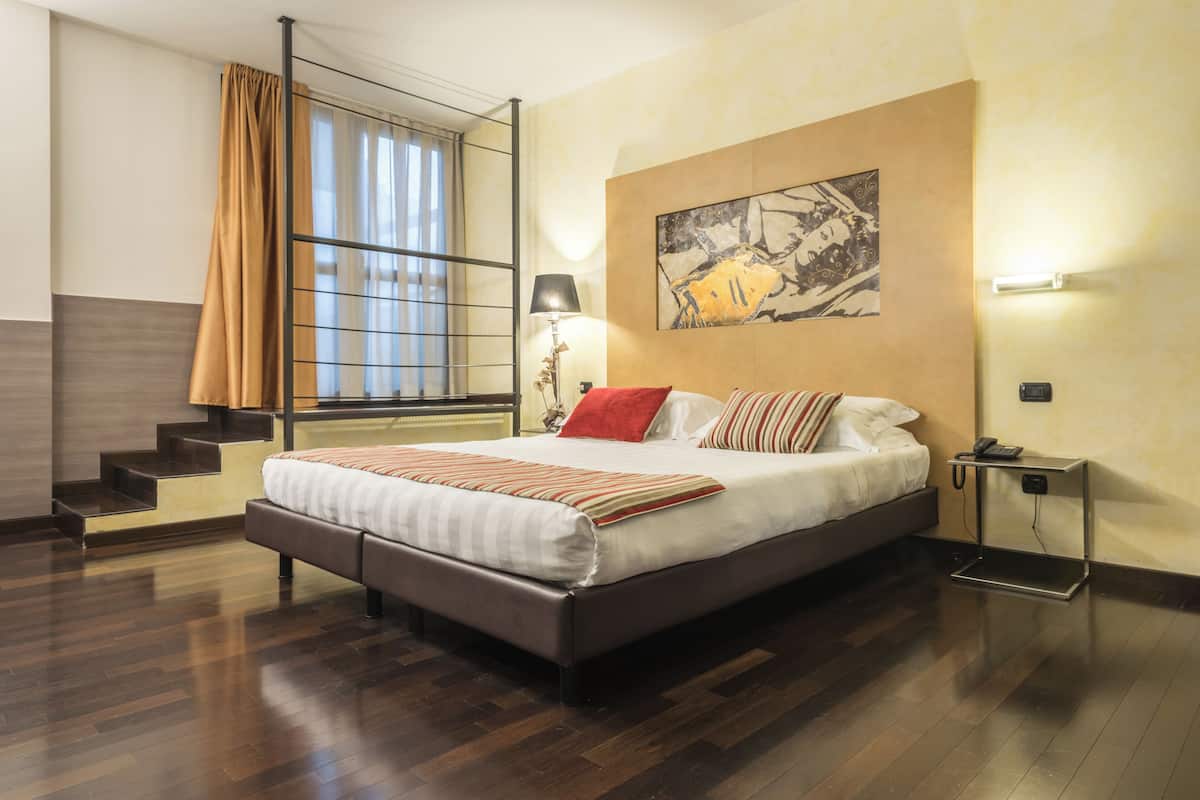 A modern bedroom with a large bed, a window with curtains, a staircase, and a painting on the wall.