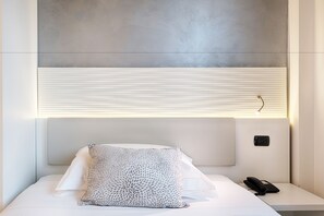 Ein modernes Hotelzimmer mit einem Bett, einem Nachttisch, einem Telefon und einer Bedienkonsole an der Wand.