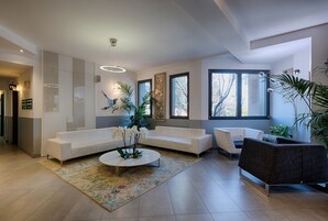 Una sala de estar moderna con un sofá blanco, un sillón oscuro, una mesita de centro y un ventanal que ofrece luz natural.