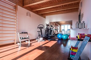 Ein geräumiges Fitnessstudio mit Holzböden, Trainingsgeräten und einem großen Fenster, das viel Tageslicht hereinlässt.