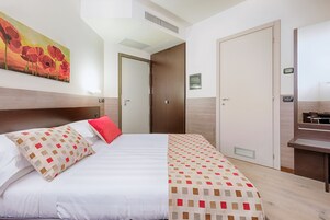 Una habitación de hotel con cama, un cuadro, un escritorio y una puerta.