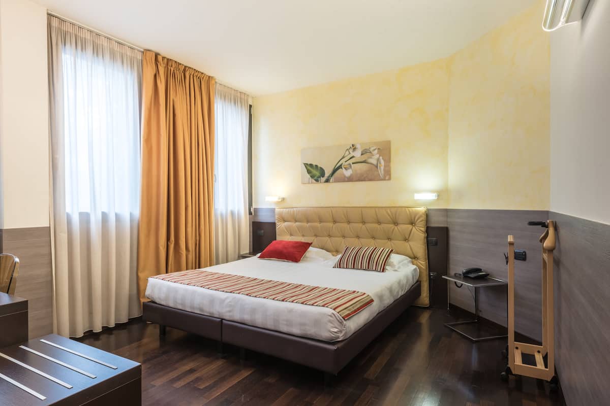 A hotel room with a large bed, a desk, a chair, a nightstand, and a painting on the wall.