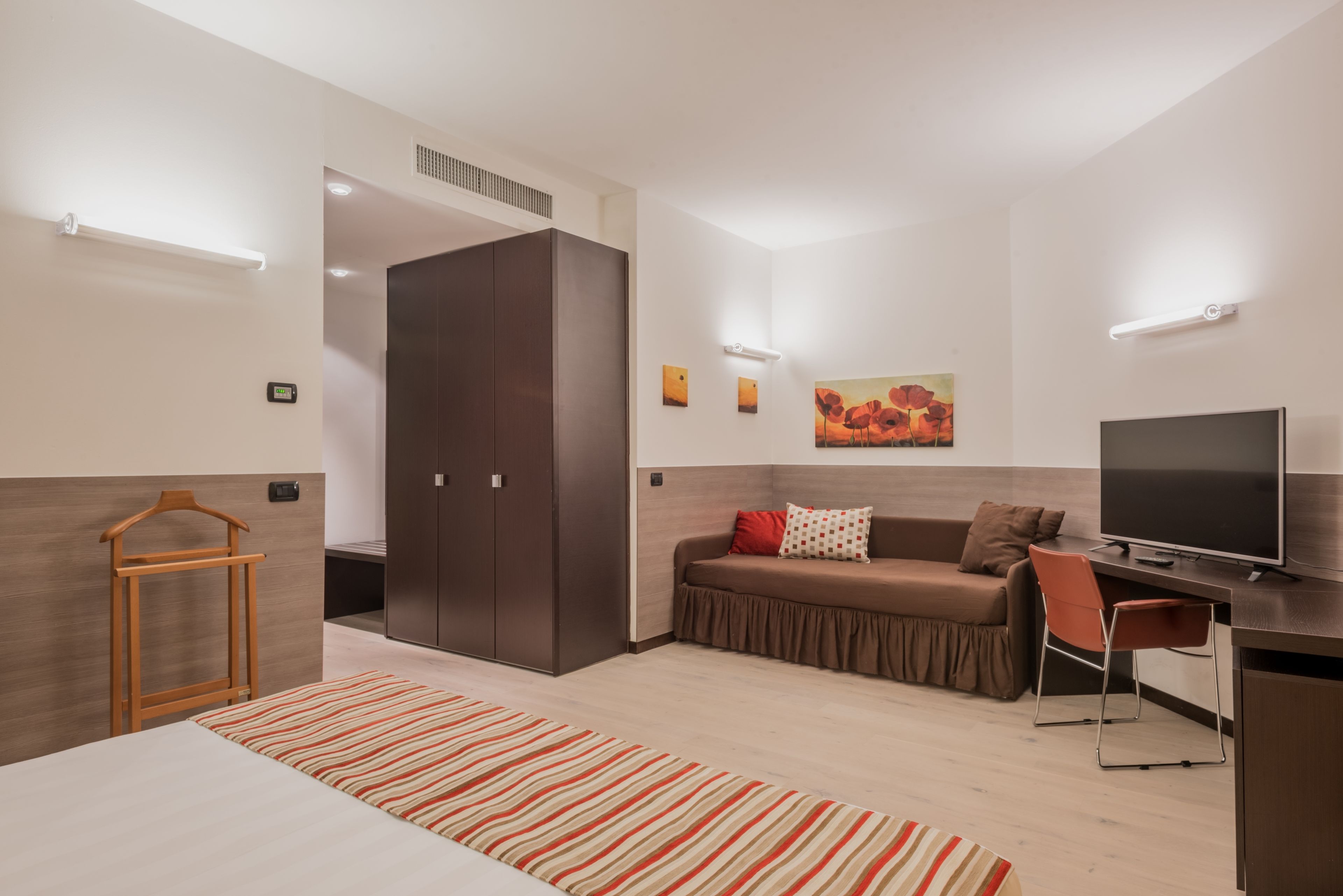 A modern hotel room with a bed, a sofa, a desk, and a TV.