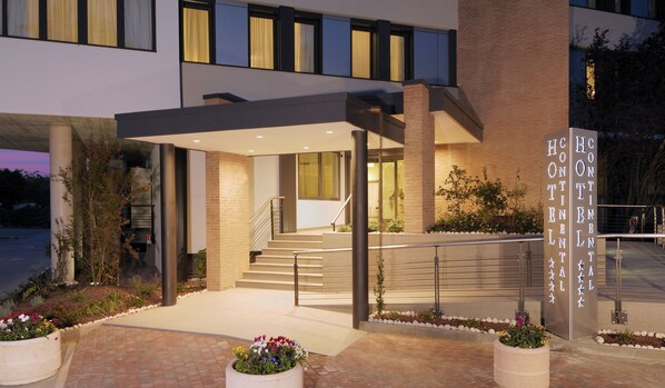 A modern hotel entrance with a covered walkway, a staircase, and a sign with the hotel's name.