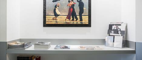 A gallery with a painting of a couple holding umbrellas, surrounded by books and magazines on shelves.