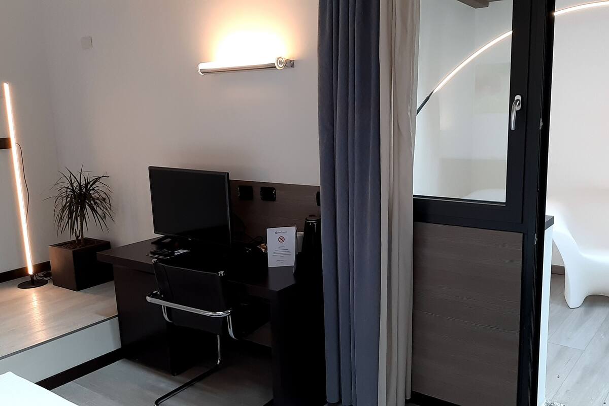 A modern hotel room with a desk, chair, and a potted plant.