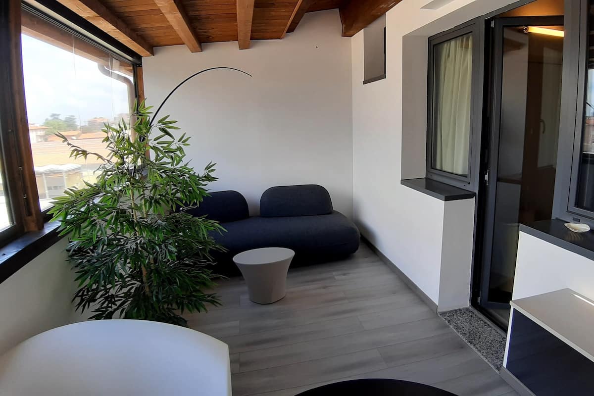 A modern balcony with a dark blue sofa, a small round table, and a large potted plant.
