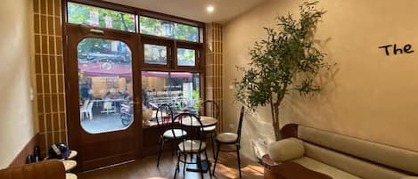 An interior with a wooden floor, a sofa, a table, chairs, and a large window with a view of the outside.