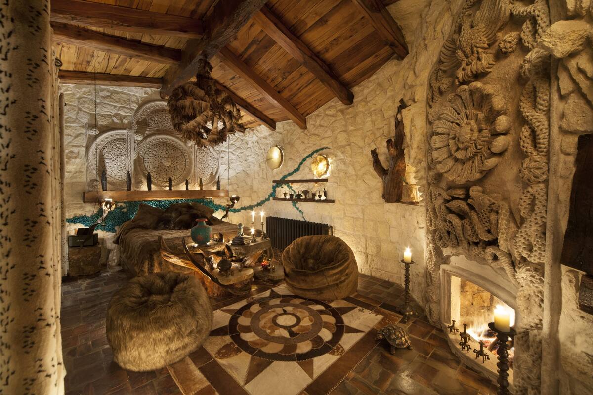 Un intérieur rustique avec des murs en pierre, des poutres en bois, une cheminée et un tapis à motifs.