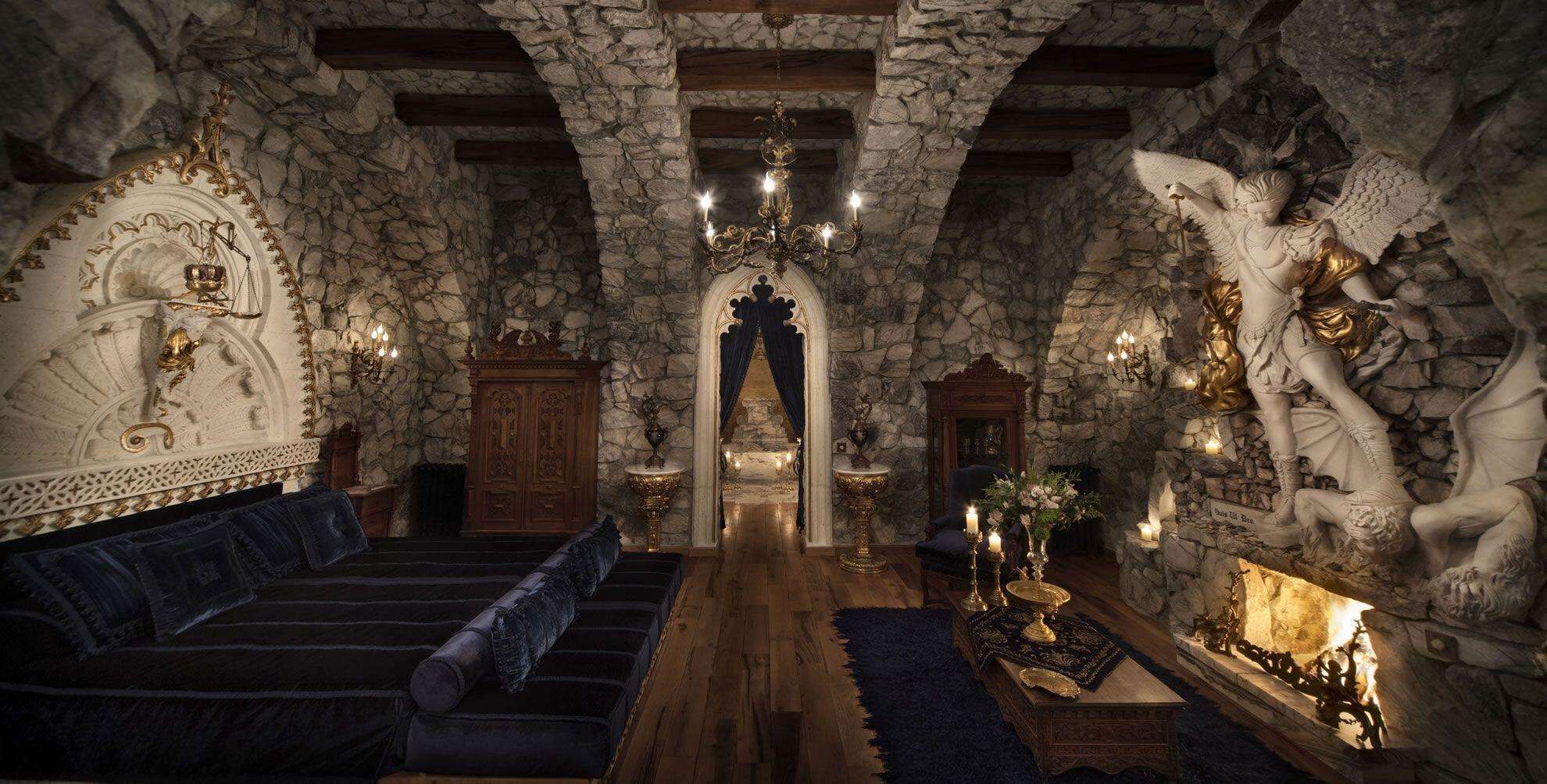 Una habitación de paredes de piedra con un banco de madera, una araña y una estatua de un ángel.