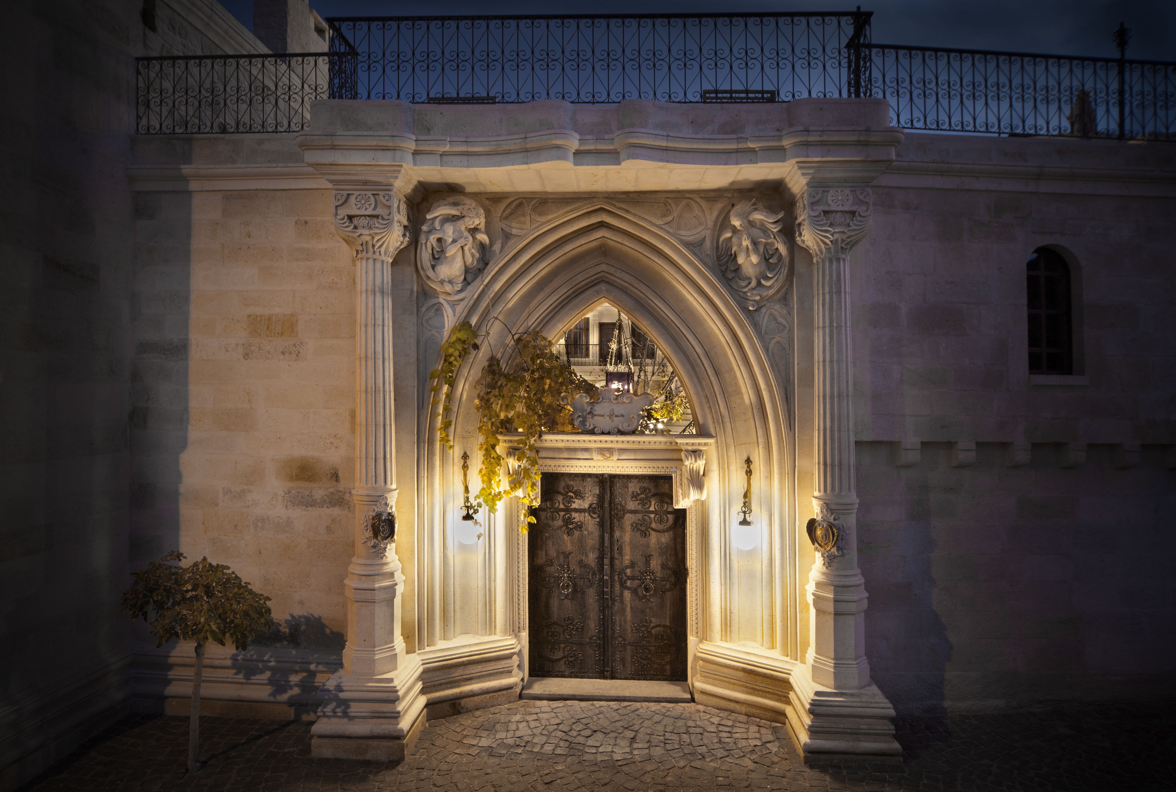 Una entrada de piedra con una puerta de madera oscura, columnas ornamentadas y un balcón de hierro forjado.