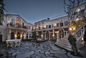 A courtyard with stone flooring, outdoor seating, and classical architecture. - Sacred House (Ürgüp)