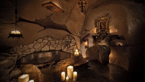 Interior rústico com parede de pedra, um banco de madeira e várias velas acesas.