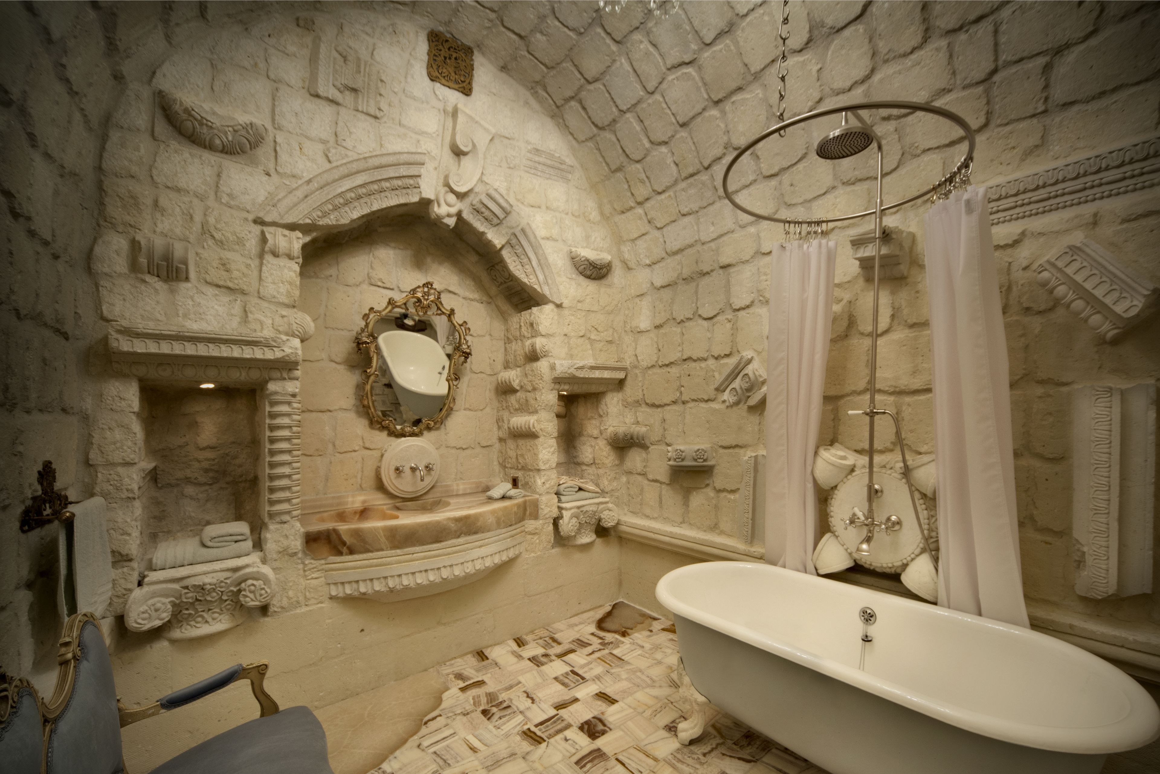 A bathroom with a stone wall, a freestanding bathtub, a sink with a mirror, and a shower area.