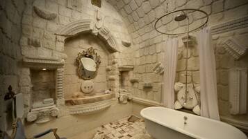 A bathroom with a stone wall, a freestanding bathtub, a sink with a mirror, and a shower area.