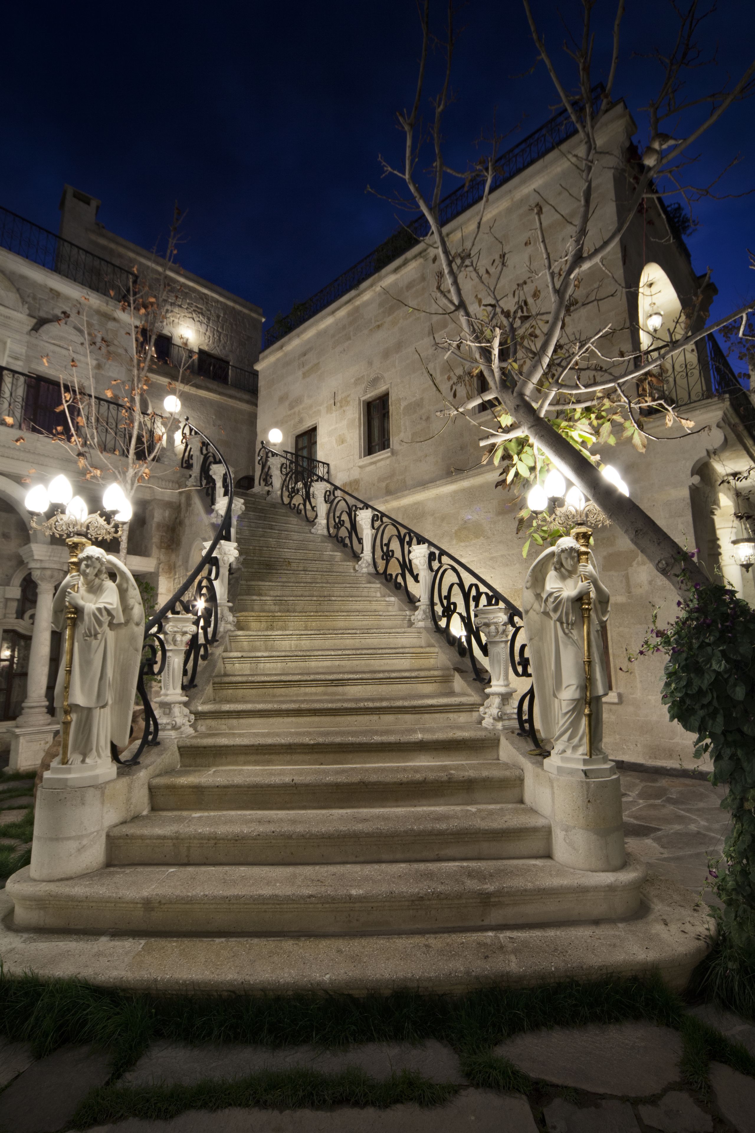 Una majestuosa escalera con barandillas ornamentadas y estatuas en la parte superior, que conduce a un edificio de arquitectura clásica.