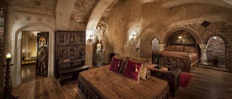 A room with a large bed, wooden furniture, and a stone wall.