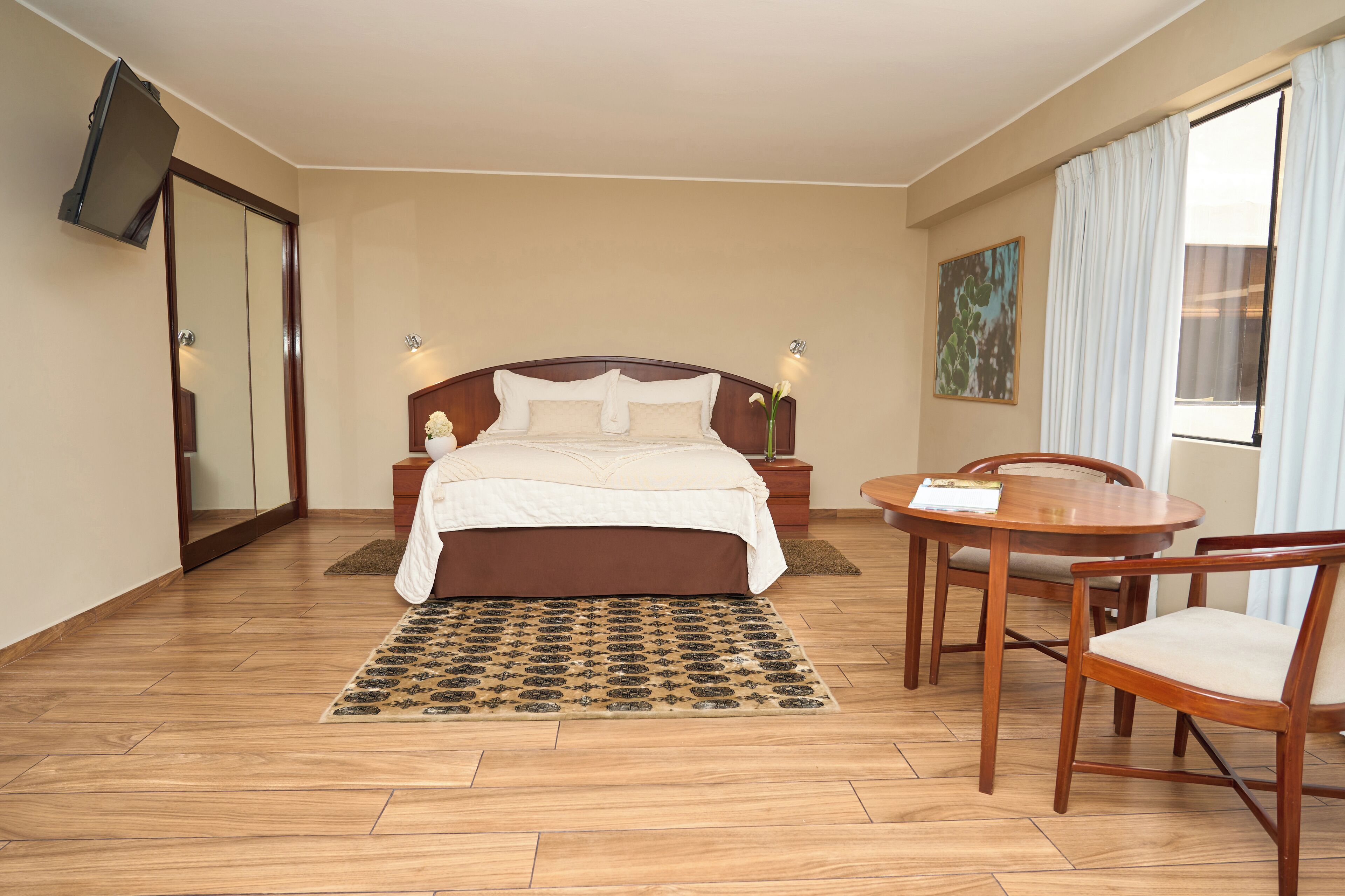 Una habitación de hotel con una cama, una mesa de comedor con sillas, un televisor y un cuadro en la pared.