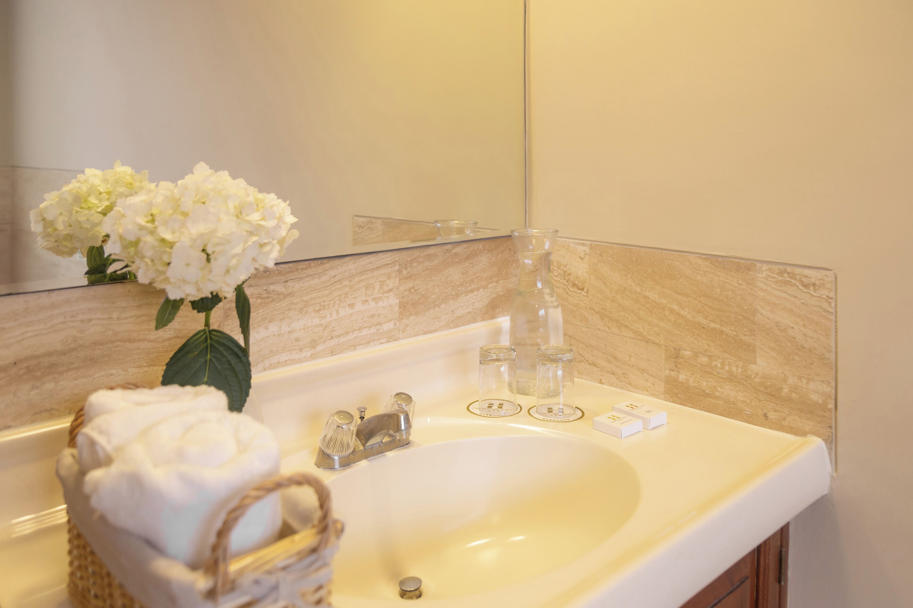 Un baño con lavamanos blanco, espejo y un jarrón de flores blancas.