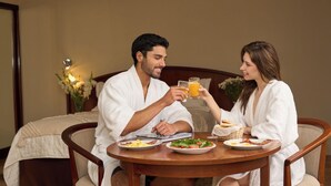 A couple in white robes sitting at a wooden table with breakfast plates, a glass of orange juice, and a notebook. - Hotel Park Suites (Lima)