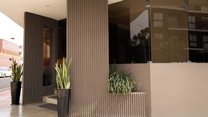 A modern building entrance with vertical paneling, potted plants, and a glass facade reflecting nearby buildings. - Hotel Park Suites (Lima)